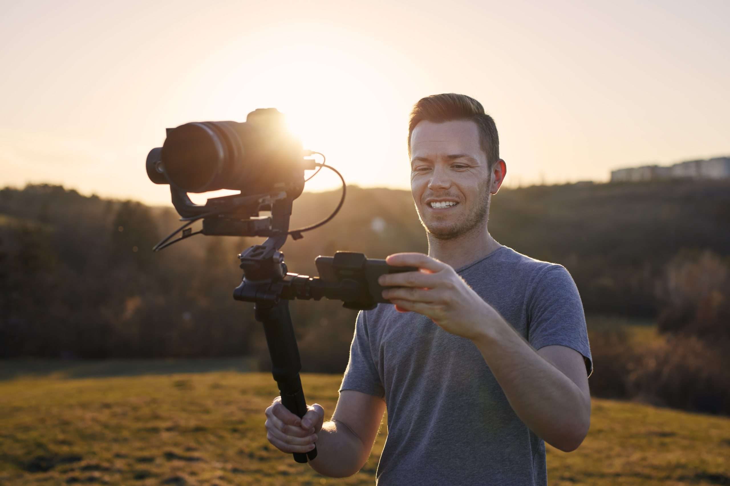 A man holding a video camera in the middle of a field.