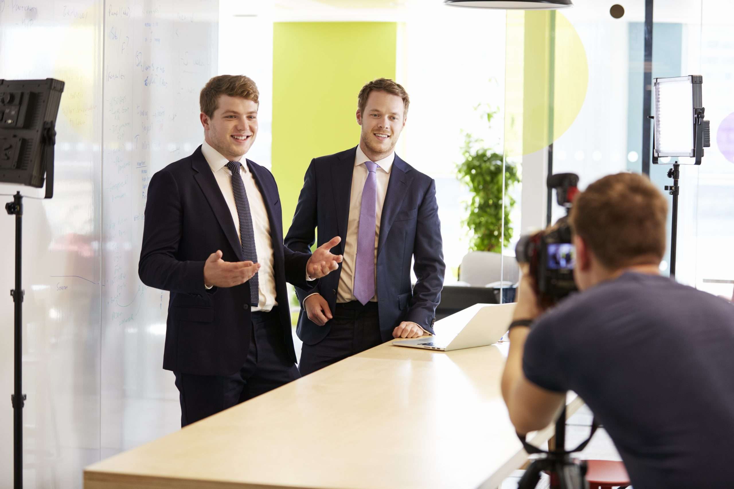 Two men in suits standing in front of a table with a camera.